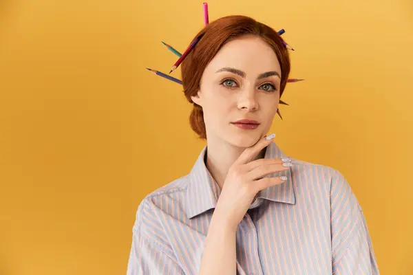 Mujer brillantemente vestida muestra un estilo artístico con lápices de colores en su cabello por una pared amarilla. - foto de stock