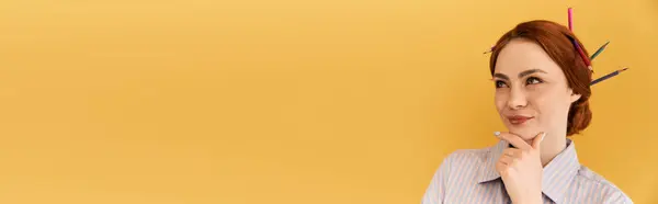 In a bright yellow space, a young woman thoughtfully ponders with pencils in her hair. — Stock Photo
