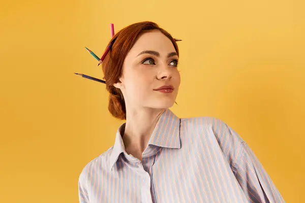 Una joven muestra juguetonamente su colorido peinado adornado con lápiz sobre un fondo amarillo. - foto de stock