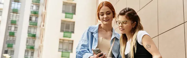 Two young women with vibrant styles chat joyfully outdoors on a sunny day near modern buildings, banner — Stock Photo