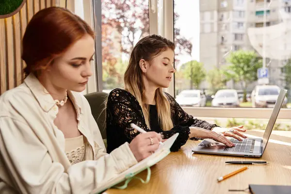 Two young women engage in remote work while enjoying coffee in a trendy cafe environment. — Stock Photo