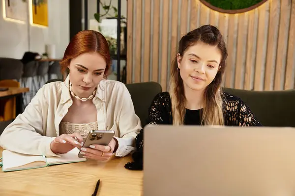 Two young women enjoy remote freelance work together in a stylish cafe, sharing ideas and tech. — Stock Photo