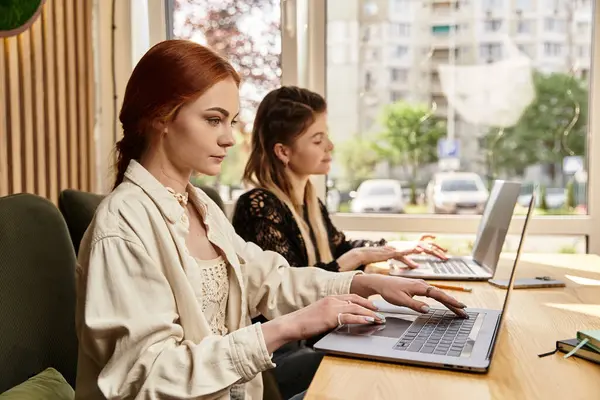 Two young women focus on their laptops while enjoying a vibrant cafe atmosphere together. — Stock Photo