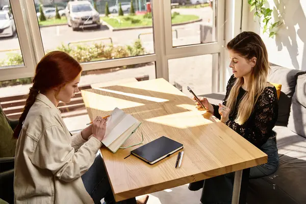 Dos amigos participan en actividades de estudio en un elegante café, con cuadernos y un teléfono sobre la mesa. - foto de stock