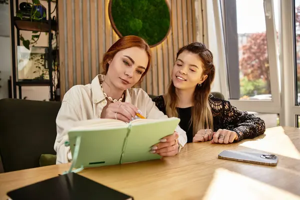 Two young women are deeply engaged in studying at a chic cafe, exchanging thoughts and notes. — Stock Photo