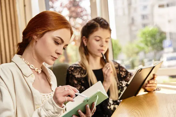 Due giovani donne si concentrano sui loro quaderni mentre studiano in un elegante caffè moderno. — Foto stock