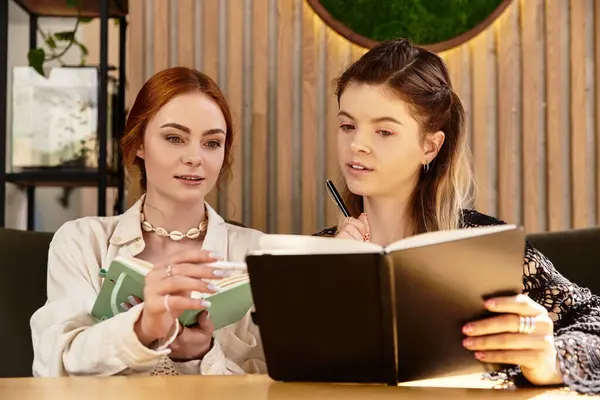 Two young women share notes and study together in a stylish, modern cafe environment. — Stock Photo