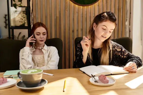 Two friends study at a stylish cafe, sharing notes and enjoying sweet treats while focused. — Stock Photo