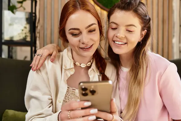 Dos amigos comparten la risa y la alegría mientras revisan sus teléfonos en un café moderno. - foto de stock