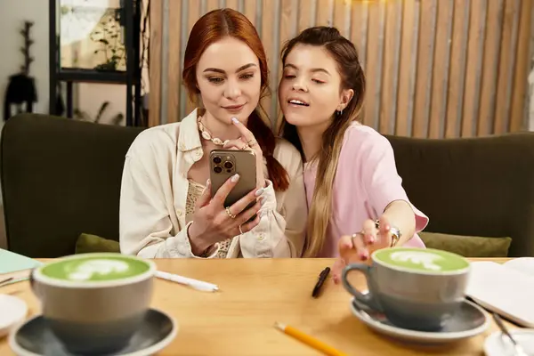 Due belle giovani donne condividono un momento mentre si godono il cappuccino matcha e usando il telefono. — Stock Photo