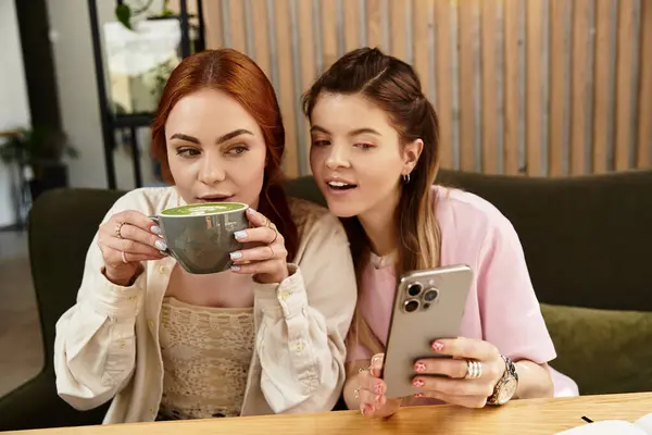 Duas jovens mulheres saboreando bebidas e compartilhando risos em um café na moda cheio de calor. — Fotografia de Stock