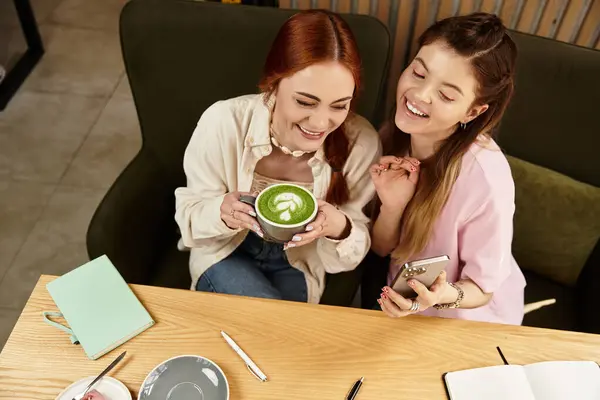 Duas jovens mulheres compartilham um momento alegre em um café chique, sorrindo e desfrutando de suas bebidas juntas.. — Fotografia de Stock