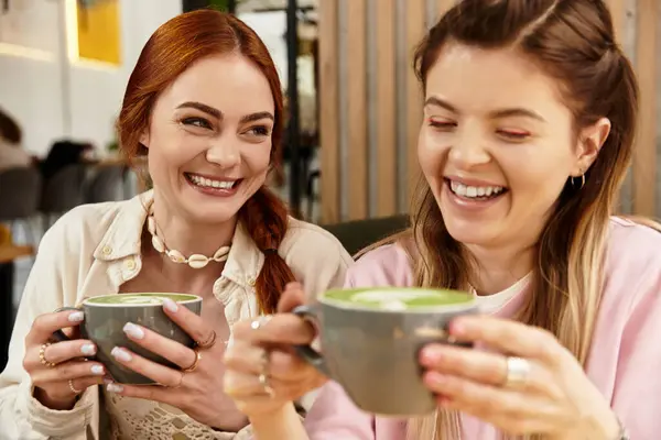 Two young women laugh and enjoy delicious drinks in a stylish cafe, creating cherished memories. — Stock Photo