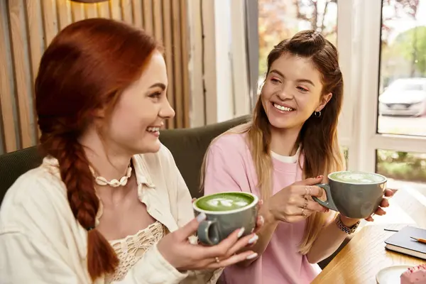 Two young women enjoy each others company while sipping green beverages in a trendy cafe. — Stock Photo
