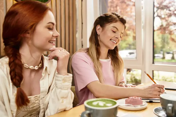 Duas jovens mulheres riem e se conectam em um café na moda, saboreando guloseimas e compartilhando ideias. — Fotografia de Stock