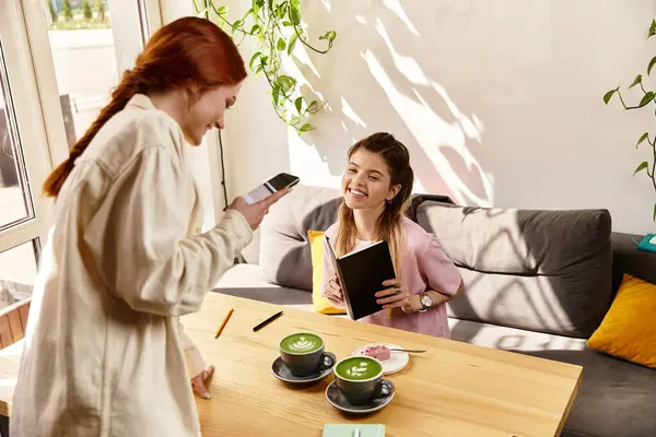 Two friends share laughs and drinks in a chic modern cafe, one woman taking photo of matcha latte — Stock Photo