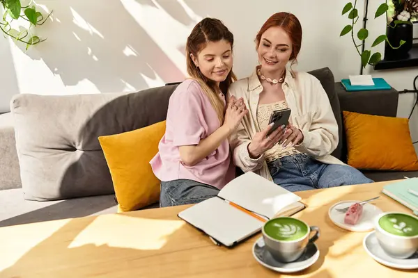Dos mujeres jóvenes comparten la risa mientras miran un teléfono en un elegante café moderno. - foto de stock