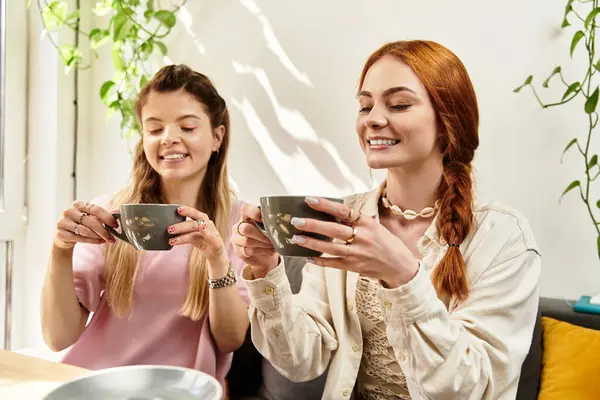 Two young women share a joyful moment over warm drinks in a vibrant cafe filled with greenery. — Stock Photo