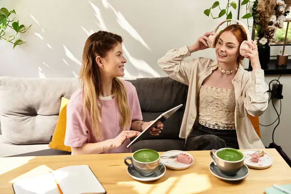Duas jovens mulheres estão compartilhando um momento alegre enquanto bebem bebidas em um café da moda. — Fotografia de Stock