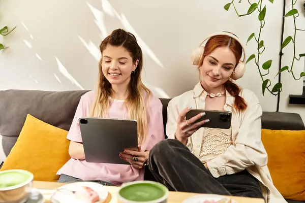 Duas jovens mulheres compartilham risos e boas vibrações ao usar tablets em um café na moda. — Fotografia de Stock
