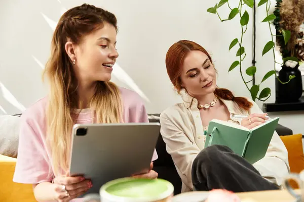 Due giovani donne si rilassano in un elegante caffè, condividendo idee e lavorando insieme ai loro compiti. — Foto stock