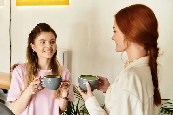 Two young women are joyfully sharing vibrant drinks in a modern, chic cafe setting. — Stock Photo