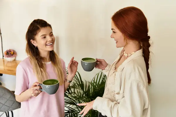 Two young women enjoy a lively conversation while holding cups in an inviting cafe atmosphere. — Stock Photo