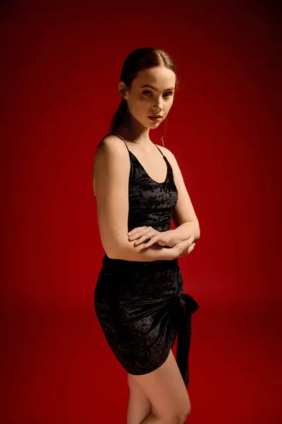Una hermosa mujer joven se levanta elegantemente en un pequeño vestido negro, mostrando aplomo y encanto. - foto de stock
