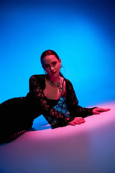A beautiful young woman showcases a trendy outfit under vibrant pink and blue lights. — Stock Photo