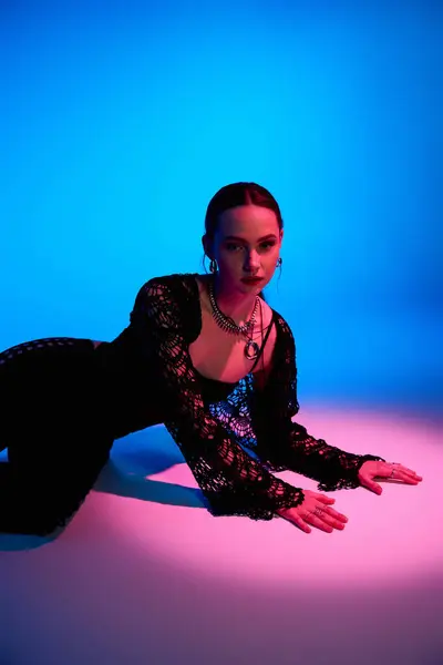 A young woman in an elegant outfit strikes a pose in a vibrant studio setting with colored lights. — Stock Photo