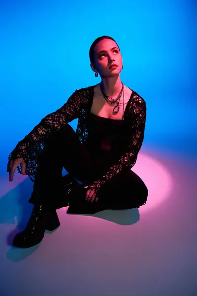 A beautiful young woman showcases her stylish outfit under pink and blue studio lighting. — Stock Photo