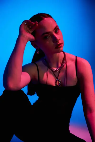 In a chic studio, a young woman models her trendy outfit with pink lighting and a blue backdrop. — Stock Photo