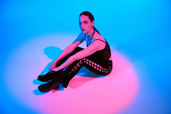 A trendy young woman poses gracefully against a blue backdrop illuminated by pink lighting. — Stock Photo