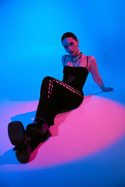 Mujer joven con estilo posa con confianza en un traje elegante, iluminado por la iluminación colorida. - foto de stock