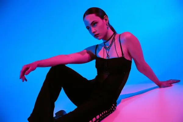 A young woman models a stylish outfit in striking pink and blue lighting. — Stock Photo