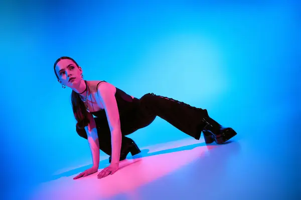 A confident young woman poses dramatically in a stylish outfit against a bright blue background. — Stock Photo