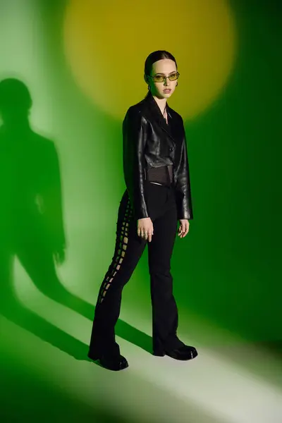 A young woman displays her fashion in a sleek black outfit against a vibrant green backdrop. — Stock Photo