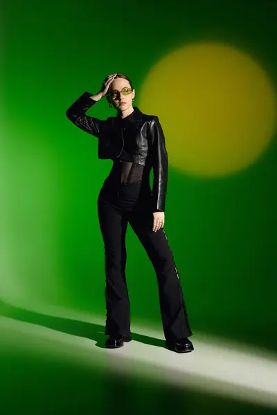 A confident young woman poses in a chic black outfit against a vibrant green background. — Stock Photo