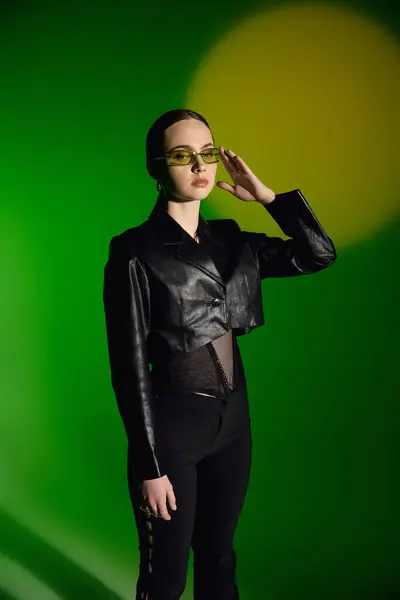 A stylish young woman in a chic black outfit poses against a green backdrop. — Stock Photo