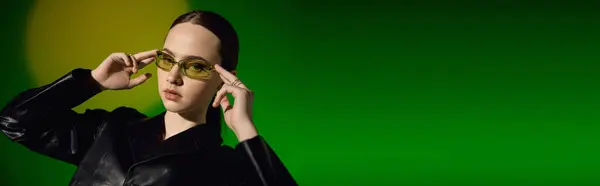 A stylish young woman models a chic black outfit against a vibrant green backdrop, banner — Stock Photo