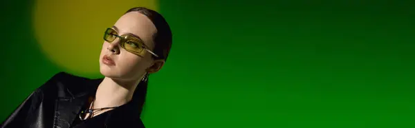 A beautiful young woman confidently showcases a chic black outfit on a stunning green background, banner — Stock Photo