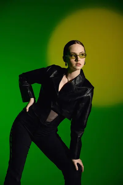 A young woman displays her fashion in a chic black outfit against a bold green backdrop. — Stock Photo