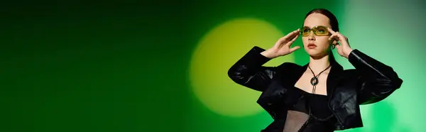 A confident young woman models her chic black outfit against a vibrant green backdrop, banner — Stock Photo