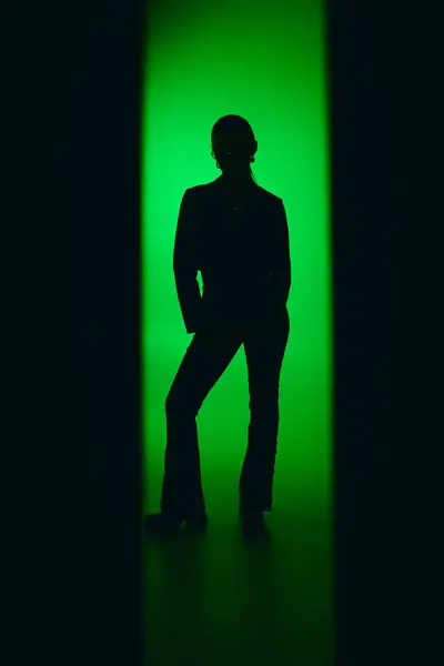 Una bella giovane donna in un elegante vestito nero posa con grazia, circondata da una luce verde vibrante. — Foto stock