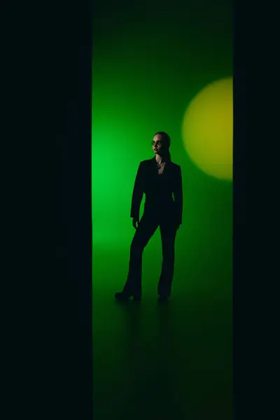 Une jeune femme confiante dans une tenue noire élégante pose sur un fond vert unique. — Photo de stock