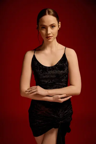 A young woman exudes elegance in her black dress against a vibrant red backdrop. — Stock Photo