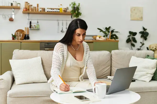 Mujer joven y elegante escribe notas para sus preparativos para el bebé, rodeada de un hogar cálido y acogedor. - foto de stock