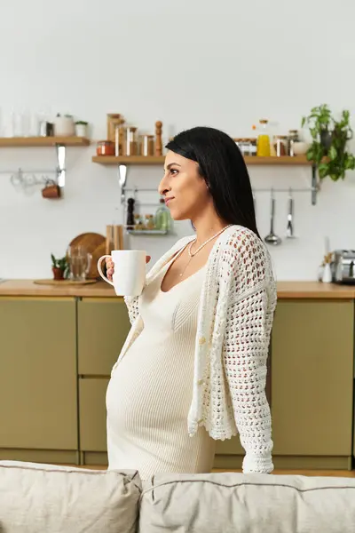 Young expectant mother stands gracefully in her cheerful kitchen, savoring a warm drink. — Stock Photo