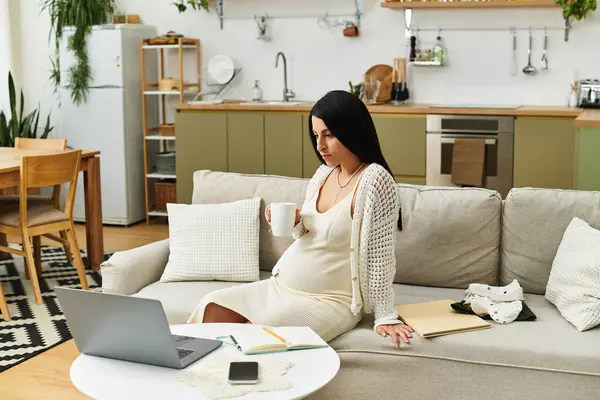 A young woman relaxes on a couch in her stylish home, enjoying a warm drink while pregnant. — Stock Photo