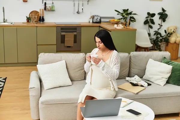 Una giovane donna, splendidamente incinta, si siede comodamente nel suo invitante spazio vitale, sorseggiando tè.. — Foto stock